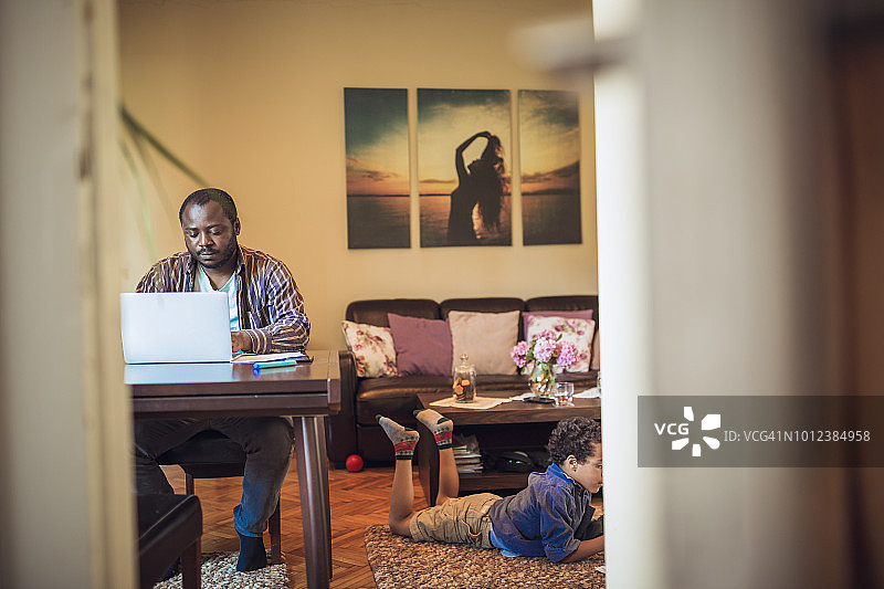 年轻男人在家工作，孩子们在玩耍图片素材