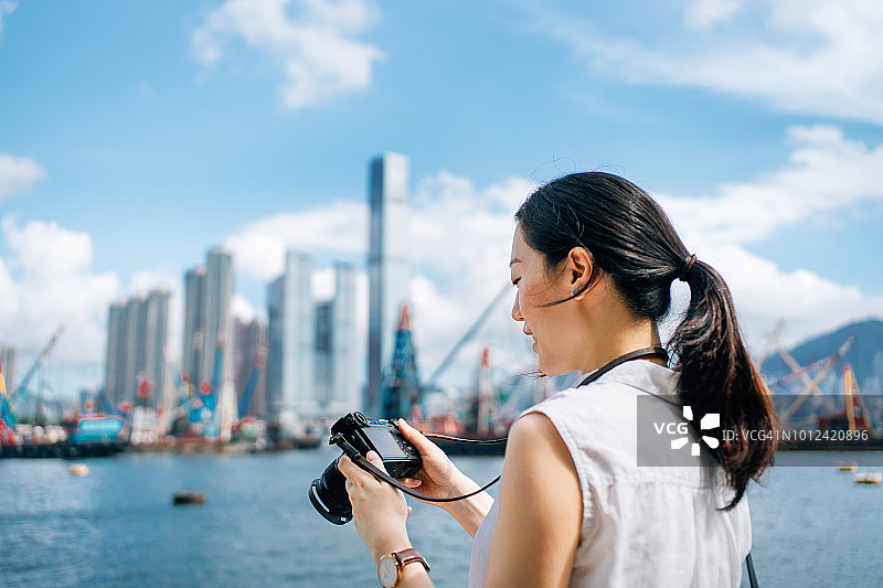 在晴朗的阳光下，用相机拍摄香港城市天际线的亚洲年轻女摄影师图片素材