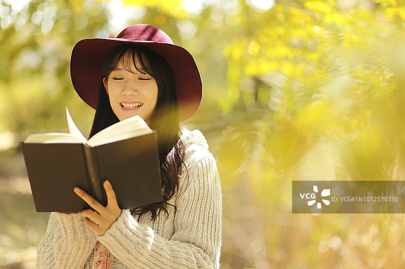 年轻女人在秋天的公园里读书图片素材