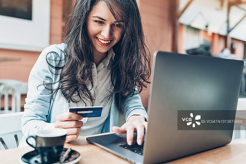 年轻女子在咖啡馆使用笔记本电脑和信用卡图片素材