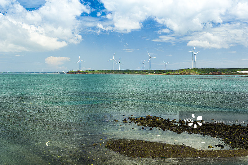 中国台湾澎湖风力发电机岛上的风车和礁石中间的岩石流入大海，反映了蓝天白云的美丽画面。图片素材