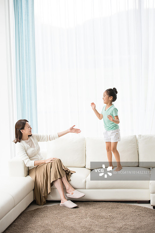 妈妈看着坐在沙发上的女儿，孩子很开心图片素材