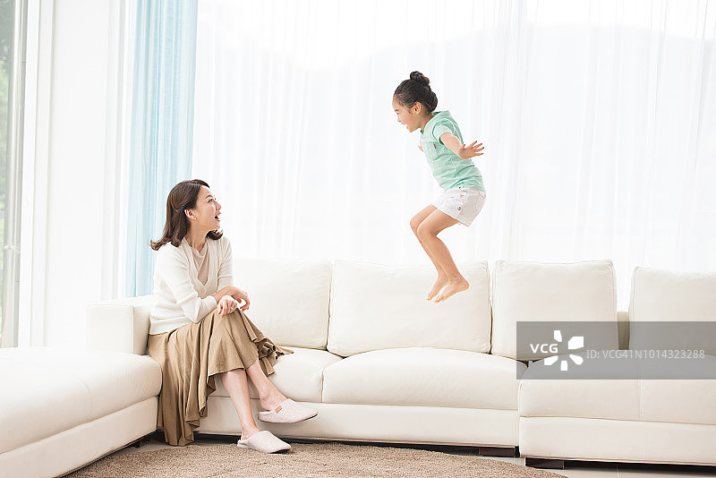 妈妈看着坐在沙发上的女儿，孩子很开心图片素材