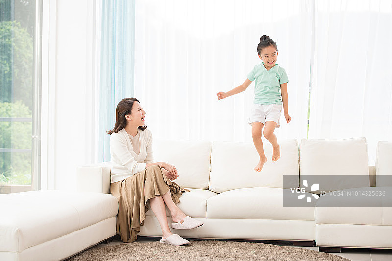 妈妈看着坐在沙发上的女儿，孩子很开心图片素材