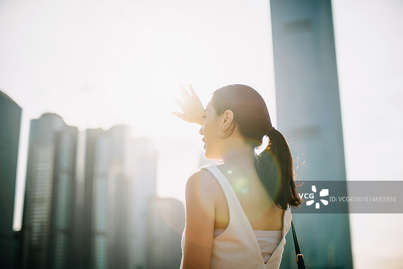 美丽的年轻亚洲女性遮挡阳光，同时俯瞰城市天际线图片素材