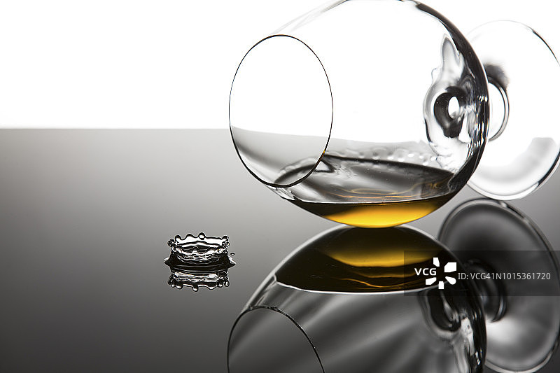 白兰地在干邑玻璃杯中侧卧于闪亮表面，水滴飞溅 - 南非工作室图片素材