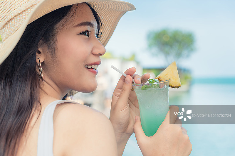在海滩上享受阳光，手持鸡尾酒的白裙年轻亚洲女性图片素材