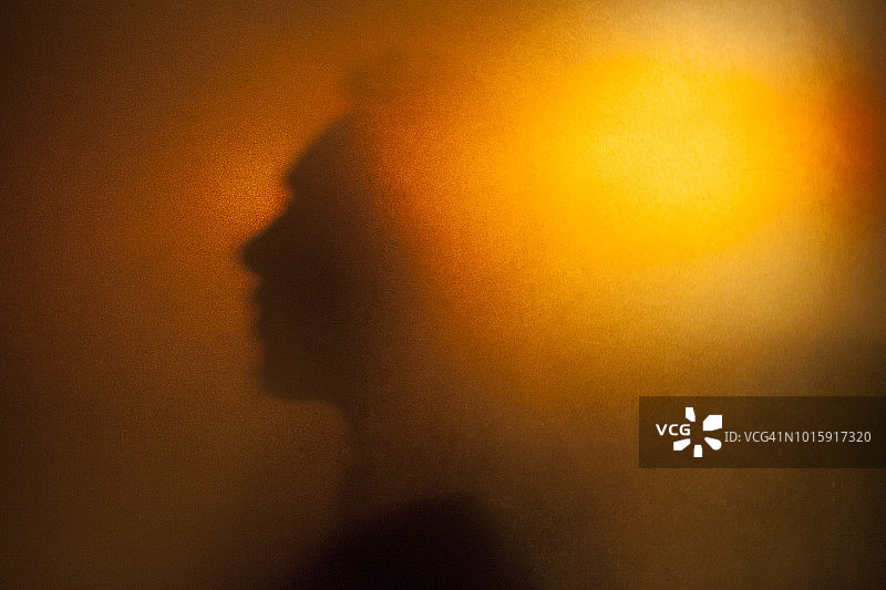橙色半透明玻璃后面的男人侧面轮廓图片素材