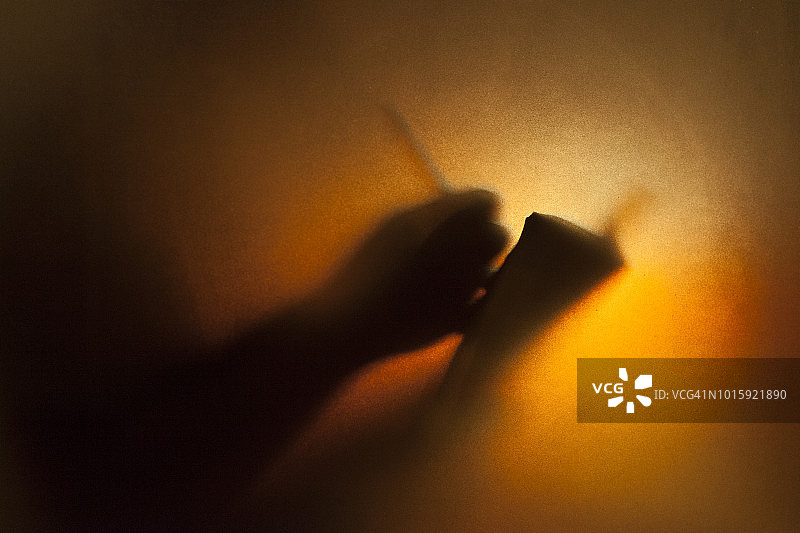 男人在温暖背景的半透明玻璃后面用笔记本写字图片素材