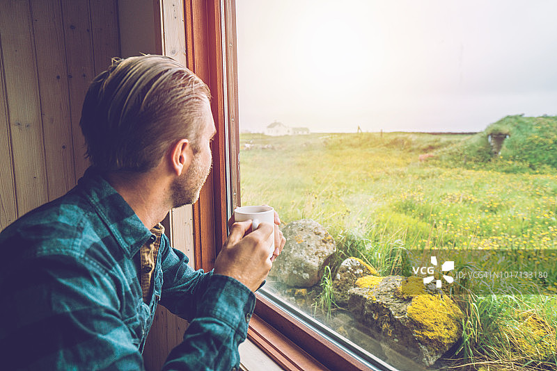 年轻男人在屋内喝咖啡并望向窗外图片素材