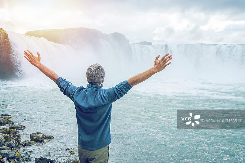 年轻男子在冰岛壮观的瀑布前伸开双臂图片素材