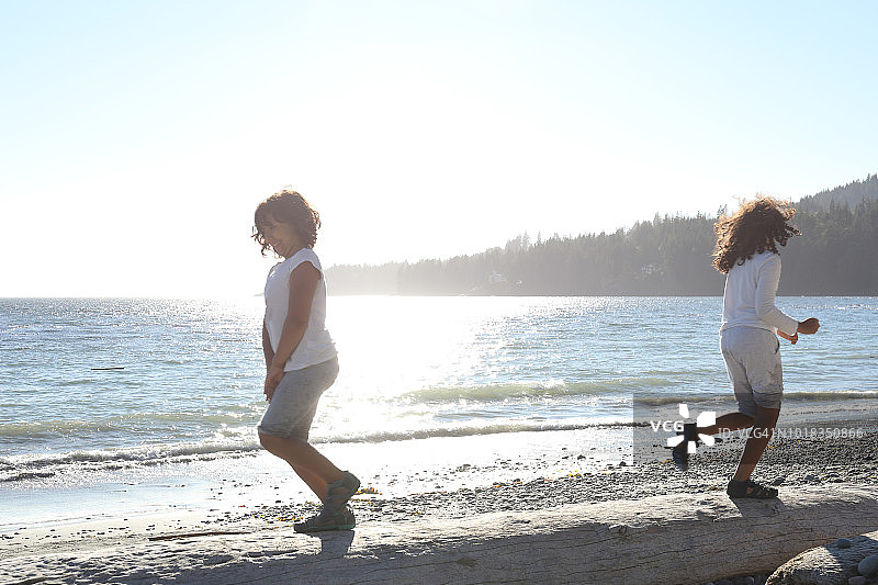 两个女孩在海滩的木头上玩童年游戏图片素材