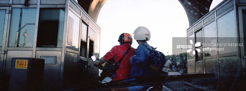 戴着头盔骑摩托车穿过意大利米兰收费站的情侣图片素材