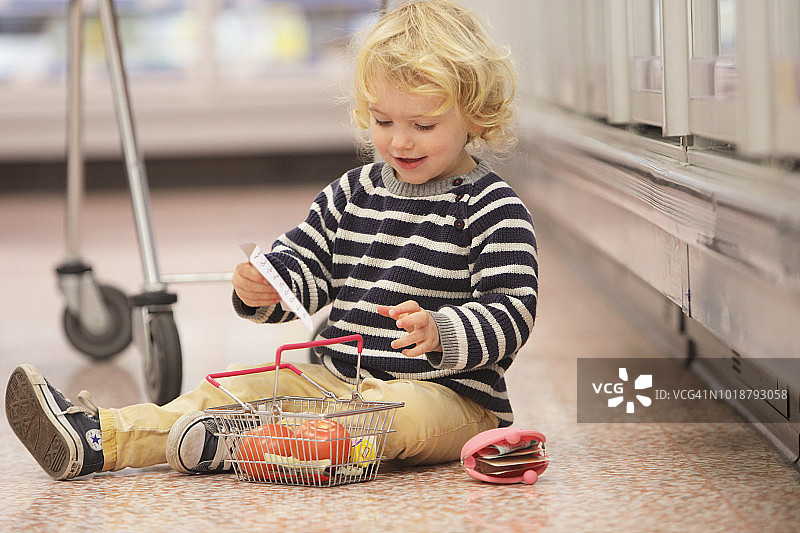 幼儿拿着清单和购物篮坐在超市的地板上图片素材