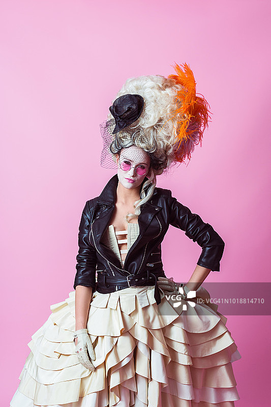 朋克巴洛克风格的女子，戴着假发和皮夹克，粉色背景图片素材