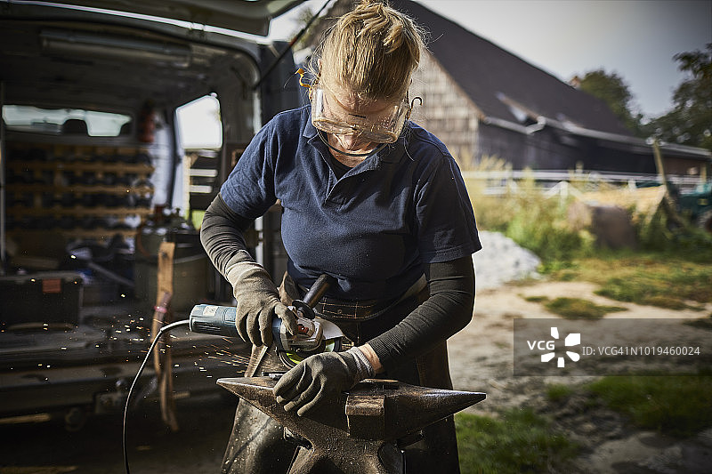 女铁匠在铁砧上用砂轮机工作图片素材