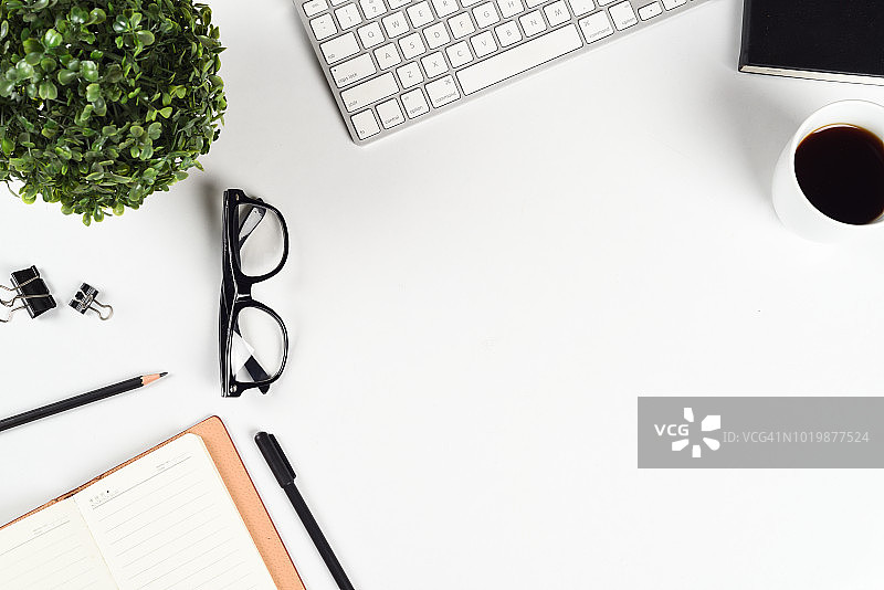 办公桌面俯视图：办公用品、电脑键盘、咖啡杯、眼镜和白色背景图片素材