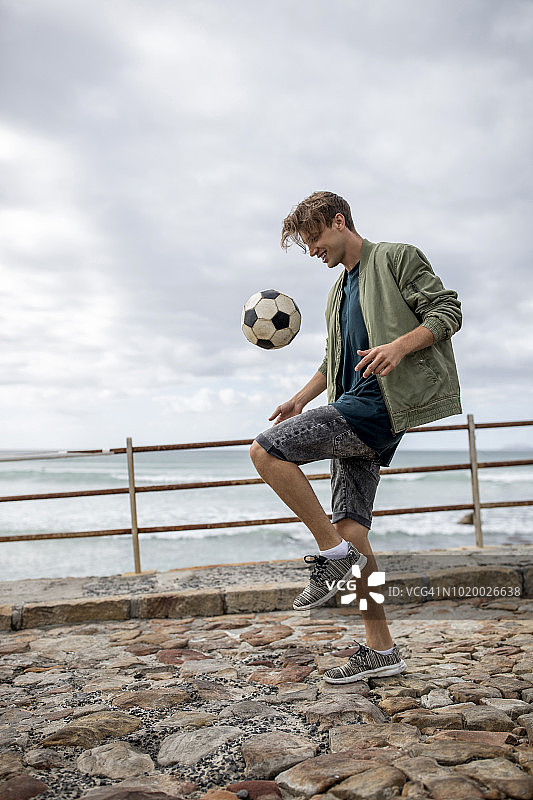 快乐的年轻男子在海边玩足球图片素材