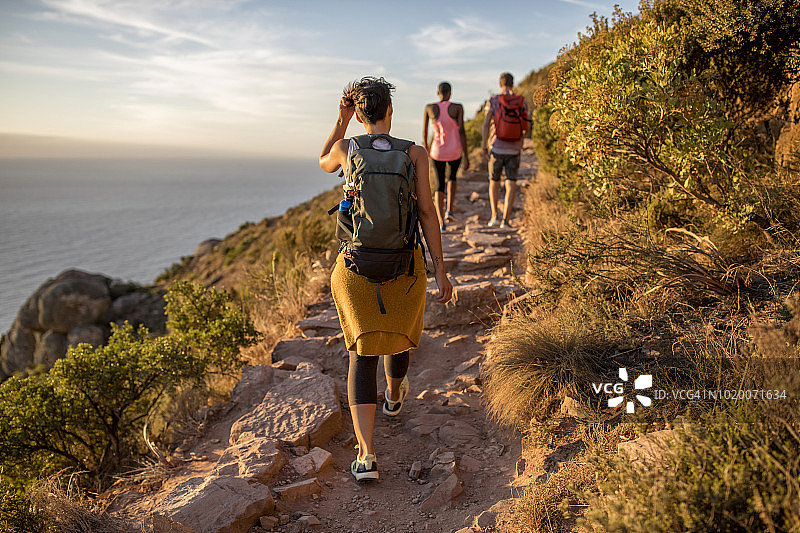在海岸山路上徒步的三位朋友背影图片素材
