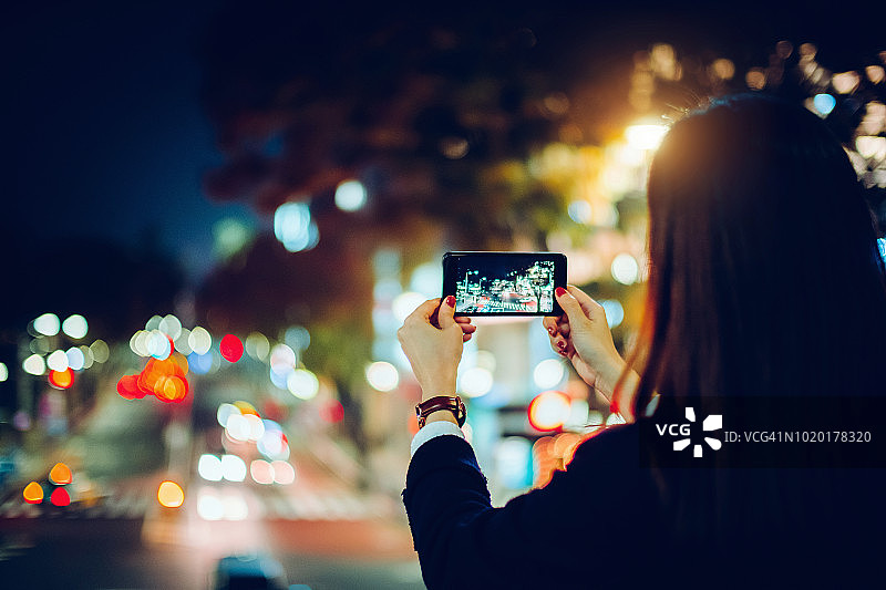在东京繁华的城市夜景中用智能手机拍照的女子背影图片素材