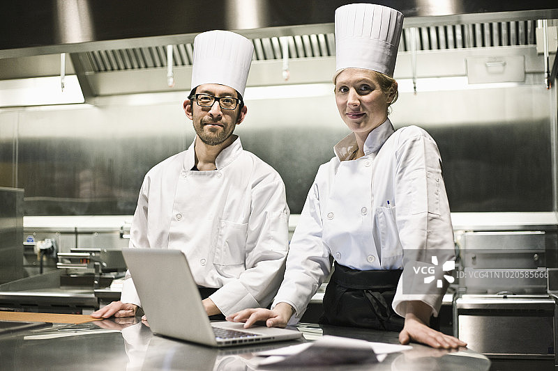 在商业厨房里用手提电脑工作的混血厨师的肖像图片素材