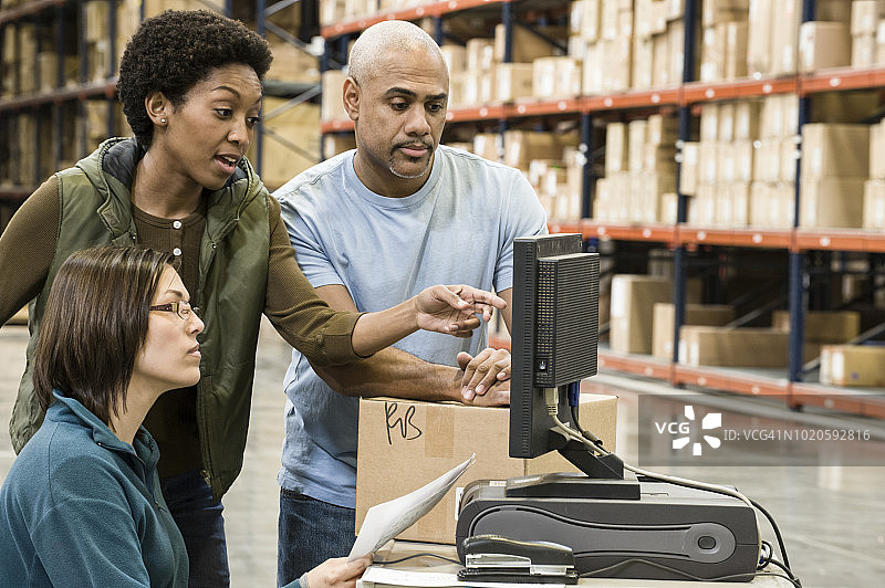 三个混血仓库工人在大型配送仓库中用电脑检查库存图片素材