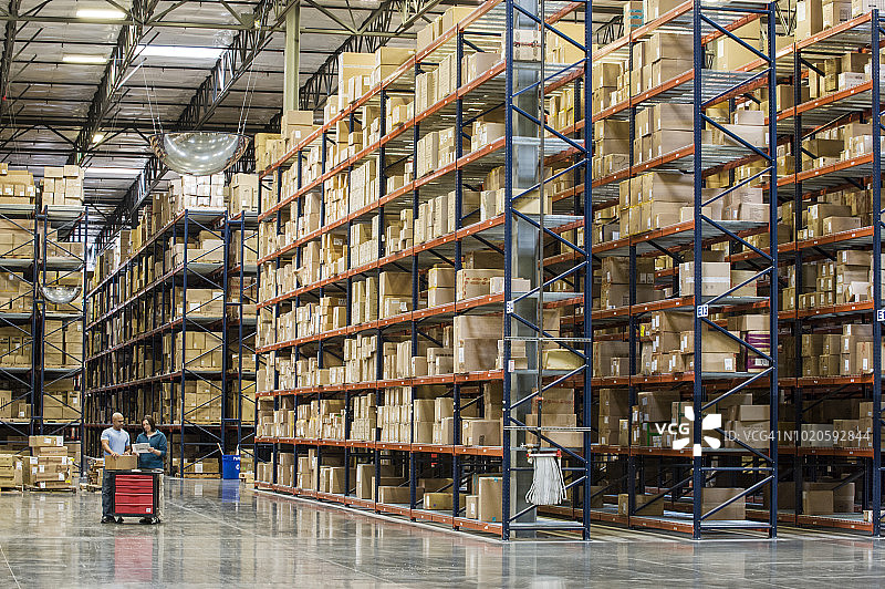 两名员工在配送仓库的临时存储区，在成排的箱子旁盘点库存图片素材