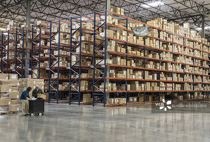两名员工在配送仓库的临时存储区，在成排的箱子旁盘点库存图片素材