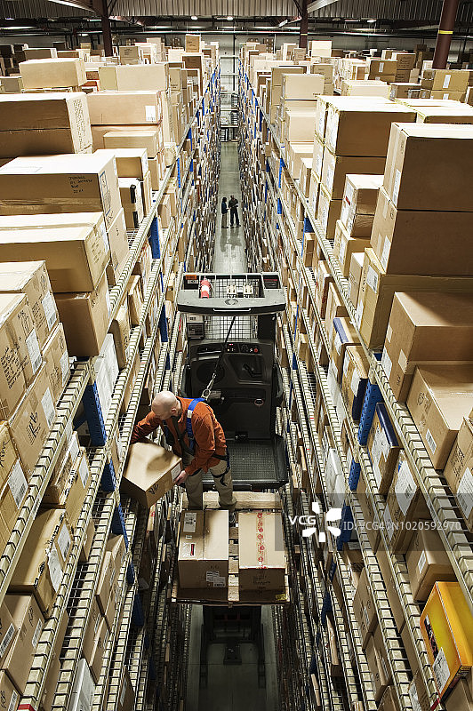 俯视：员工站在配发仓库的电动拣货机上，从架子上取出一个盒子图片素材