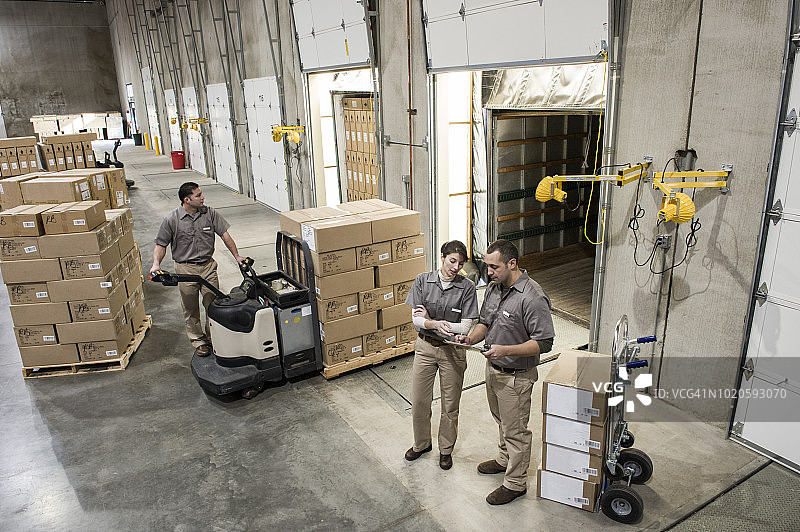 三名不同种族的仓库工人，身穿制服，将盒装产品装载到配送仓库的卡车后部。图片素材