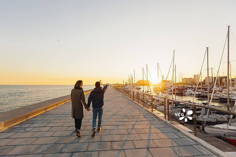 年轻情侣牵手在西班牙巴塞罗那走向日落图片素材