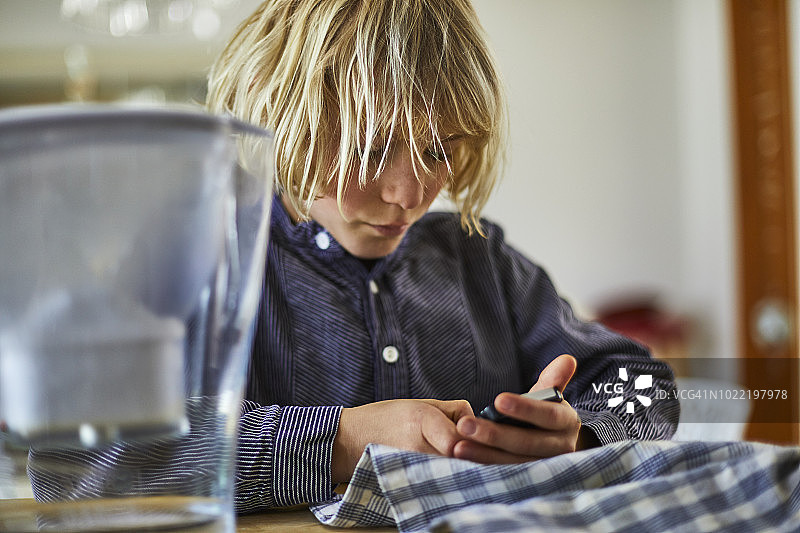 在桌旁使用手机的金发男孩图片素材