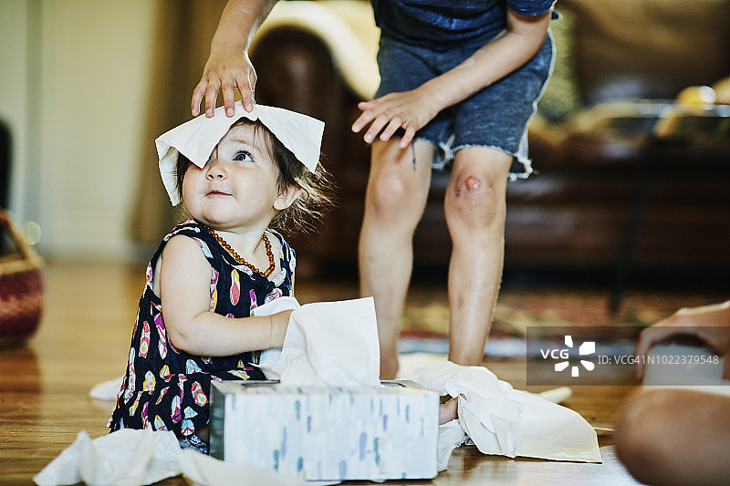在客厅里把面巾纸放在妹妹头上的男孩图片素材