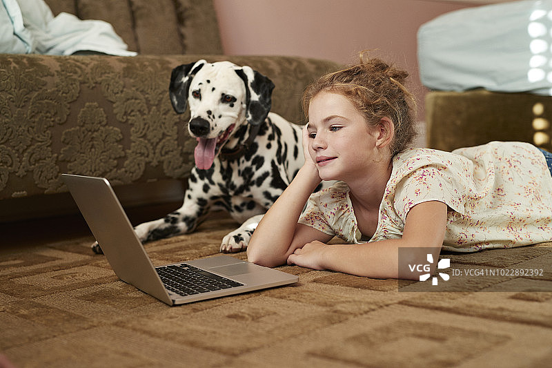 在地板上使用笔记本电脑的可爱女孩，旁边是斑点狗图片素材