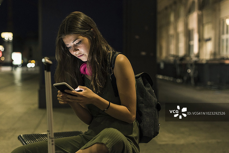 晚上，一位背着背包和行李的年轻女子正在使用手机图片素材