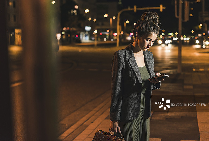 夜晚拿着皮包看手机的年轻女商人图片素材