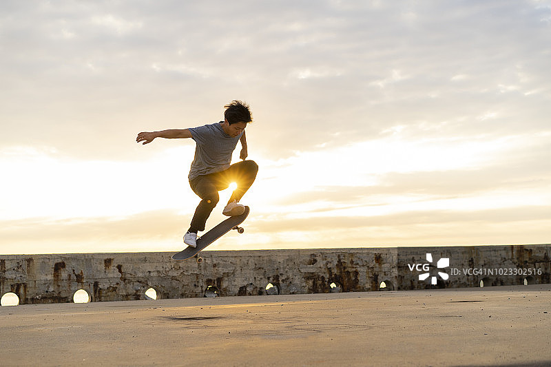 在海滩附近日出时玩滑板的中国年轻男子图片素材