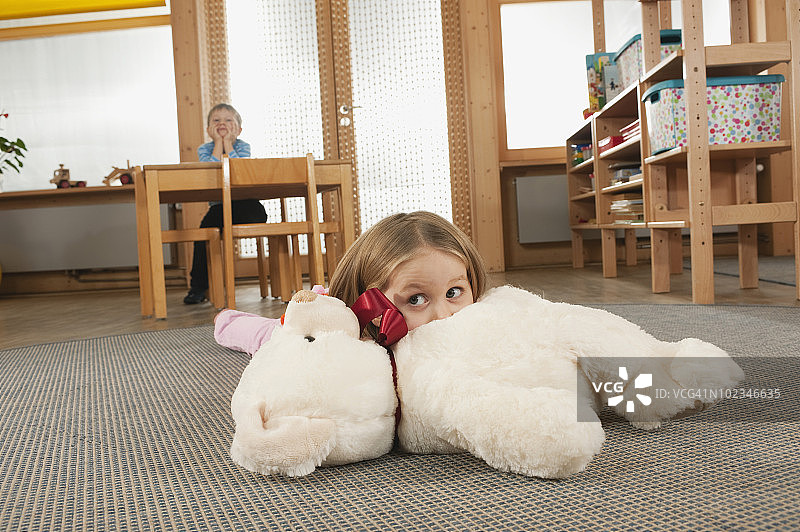 德国，幼儿园里躺在地上的3-4岁女孩，背景中4-5岁男孩坐在桌旁，手托下巴图片素材