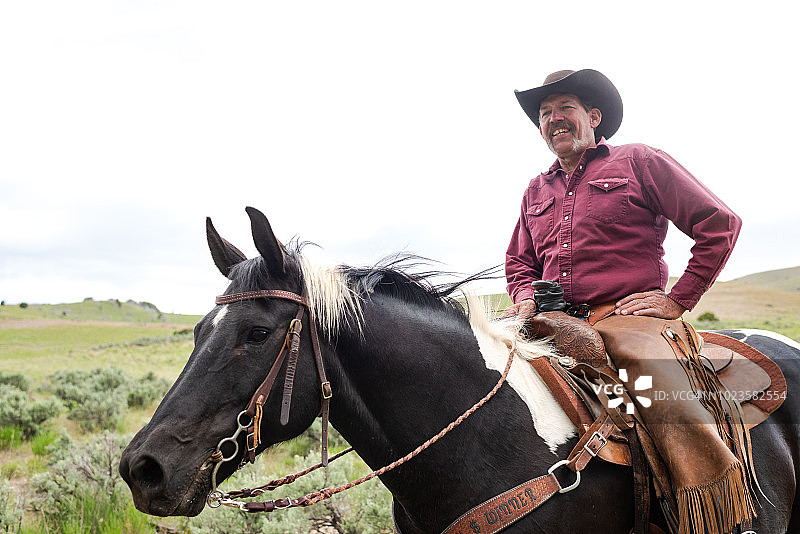 微笑的牛仔骑在马上手持鞍角低角度肖像图片素材