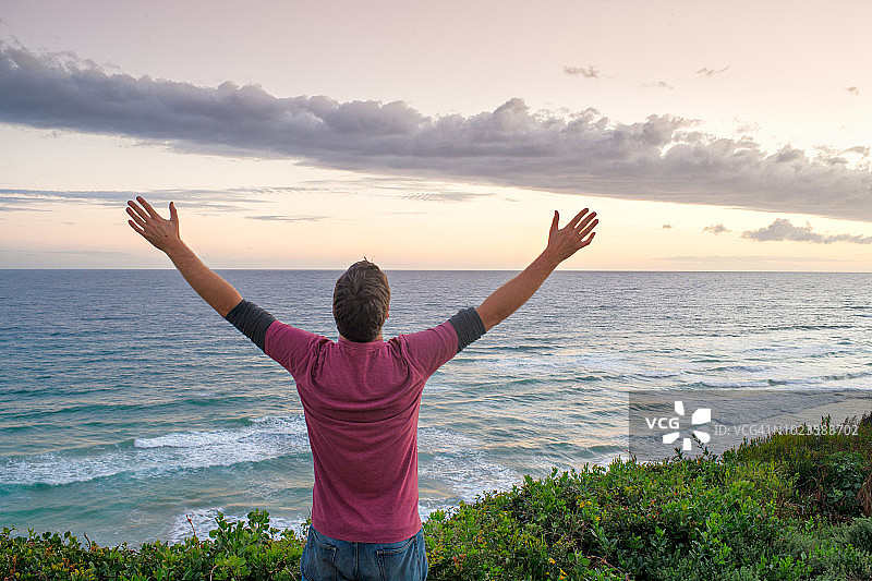 举起双臂俯瞰壮观日落和云彩的男人图片素材