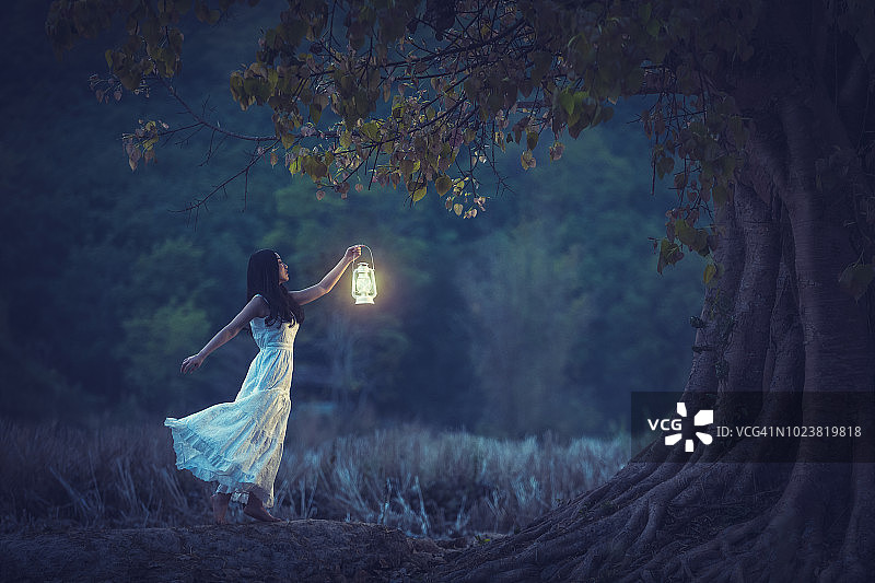 在秋天的森林里，拿着灯笼在树下闪耀的白色连衣裙美丽女孩图片素材