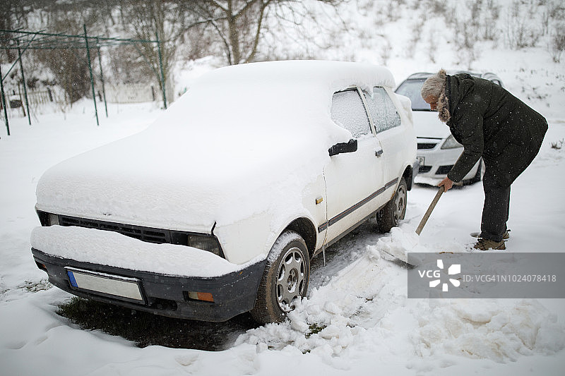 被困在雪中，老年人用铲子除雪图片素材