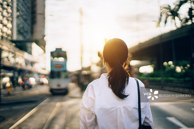 女子在城市等待交通工具的背影（日落时分）图片素材
