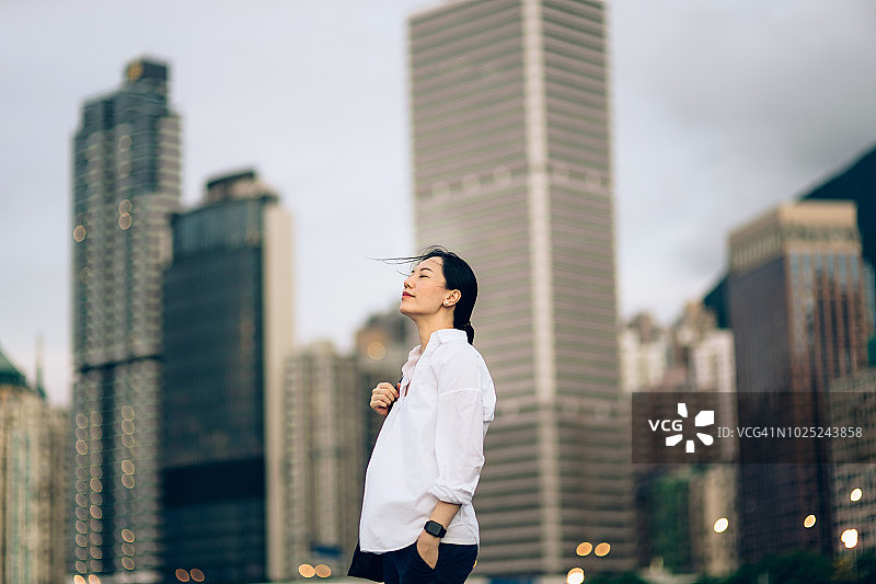 在城市天际线下享受宁静和微风的闭着眼睛的年轻女子图片素材