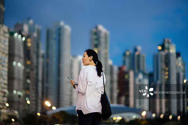自信的女商人在金融区使用手机，背景是黄昏时灯火通明的城市图片素材