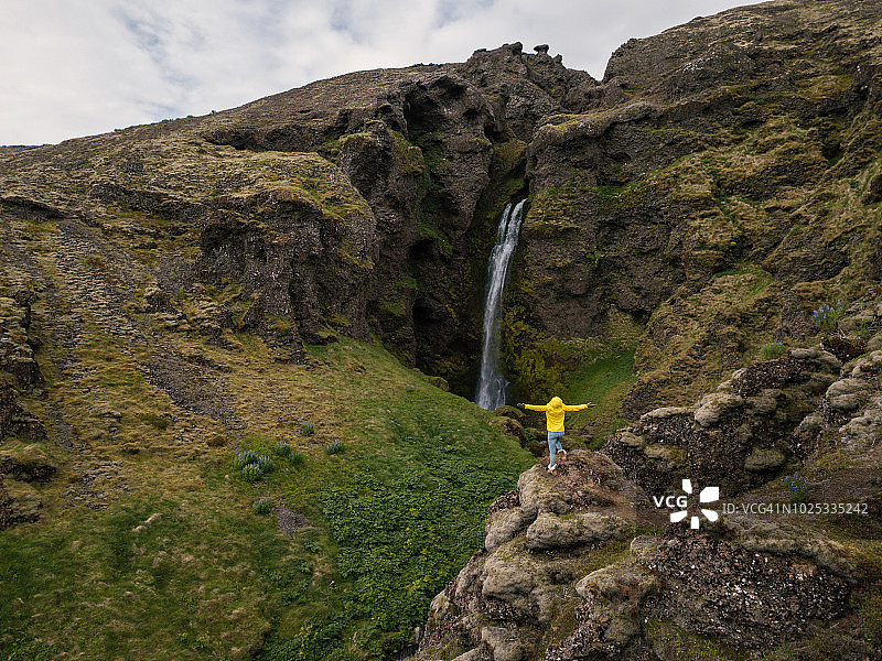 冰岛壮观瀑布前伸展双臂的年轻女子无人机航拍图片素材