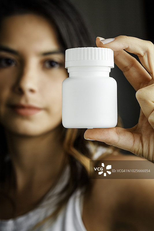 拿着白色塑料药瓶的西班牙裔年轻女子图片素材