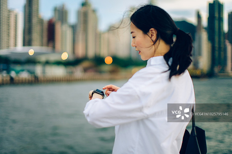 年轻女商人查看智能手表上的行程安排，背景是海港城市景色图片素材