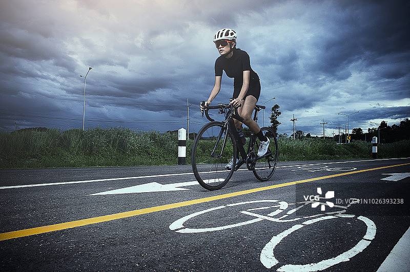 戴头盔的亚洲健康女孩在自行车道上骑行锻炼图片素材