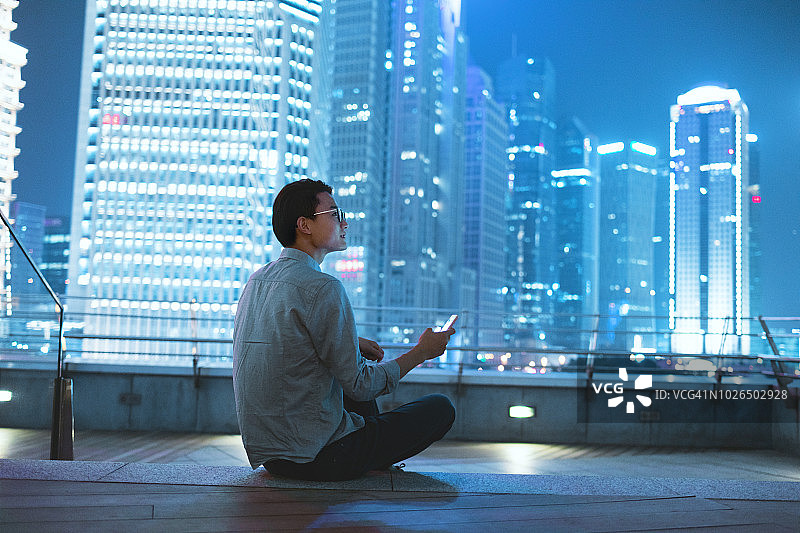 在屋顶上看智能手机的年轻商人图片素材